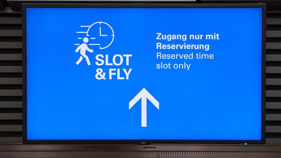 Ein Screen mit der Aufschrift "Slot&Fly - Zugang nur mit Reservierung" ist am Hamburger Flughafen zu sehen. © picture alliance / dpa Foto: Georg Wendt