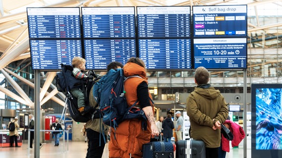 Reisende blicken auf eine Anzeigetafel am Hamburger Flughafen. © Markus Scholz/dpa 