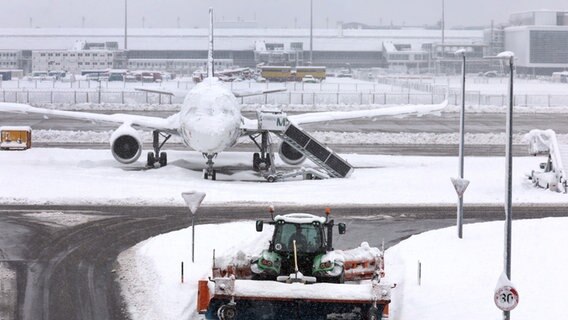 Ein Schneeräumer fährt im Schneetreiben auf dem Münchner Flughafen vor einer Maschine entlang. © picture alliance / dpa Foto: Karl-Josef Hildenbrand