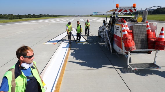 Mitarbeiter des Wartungs- und Instandhaltungsteams erneuern die Markierungen auf einer der beiden Start- und Landebahnen am Hamburger Flughafen. © picture alliance/dpa Foto: Christian Charisius