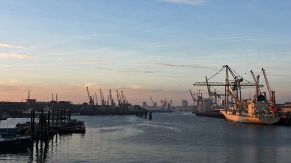 Im Abendrot geht der Blick von der Veddeler Chaussee auf die Hamburger Skyline, davor liegt ein Schiff, links sind die historischen und rechts moderne Hafenanlagen zu erkennen. © NDR Foto: Daniel Sprenger