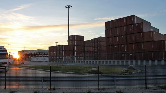 Die Sonne geht hinter hochgestapelten Containern im Freihafen unter. © NDR Foto: Daniel Sprenger