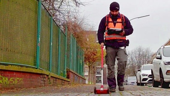 Ein Mitarbeiter von Gasnetz Hamburg geht auf einem Bürgersteig, sucht nach Lecks und kontrolliert Daten auf einem Tablet. © Gasnetz Hamburg 