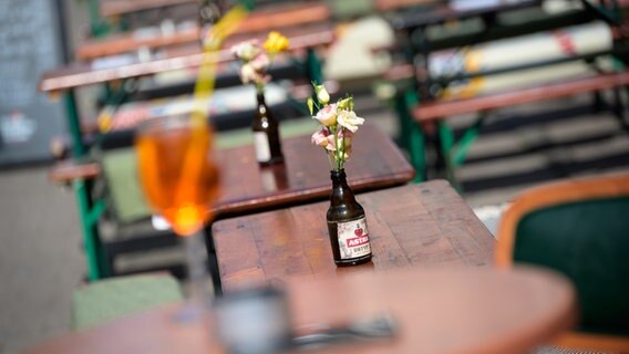 Bierflaschen mit Blumen stehen in der Sonne auf Tischen vor einem Lokal im Schanzenviertel. © picture alliance/dpa | Jonas Walzberg Foto: Jonas Walzberg