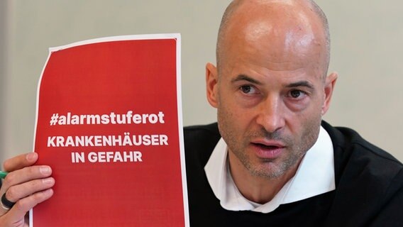 Joachim Gemmel, Vorsitzender der Hamburgischen Krankenhausgesellschaft, hält bei einer Pressekonferenz einen roten Zettel mit der Aufschrift "#alarmstuferot. Krankehäuser in Gefahr." © picture alliance / dpa Foto: Marcus Brandt