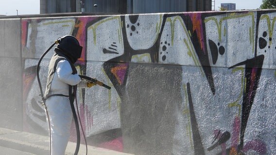 Ein Arbeiter entfernt Graffiti an einer Flutschutzmauer in Hamburg-Wilhelmsburg. © picture alliance / rtn - radio tele nord Foto: rtn, frank bründel