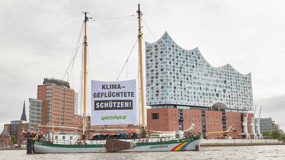 Das Greenpeace-Segelschiff "Beluga II" kreuzt mit einem Banner mit der Aufschrift "Klima-Geflüchtete schützen!" vor der Elbphilharmonie. © picture alliance/dpa Foto: Georg Wendt