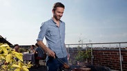Ein Mann grillt auf einer Dachterrasse. © picture alliance / Westend61 Foto: Westend61 / Rainer Berg