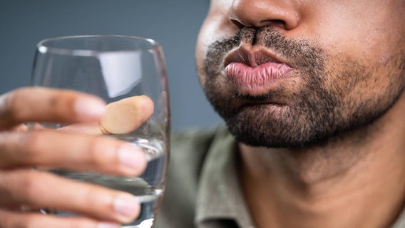 Ein Mann gurgelt mit Wasser in einem Glas. © imago images / Panthermedia 