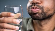 Ein Mann gurgelt mit Wasser in einem Glas. © imago images / Panthermedia 