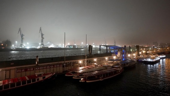 Barkassen liegen an den Landungsbrücken im Hafen. Im Hintergrund sind die Docks der Werft Blohm+Voss hell erleuchtet. © picture alliance/dpa Foto: Marcus Brandt