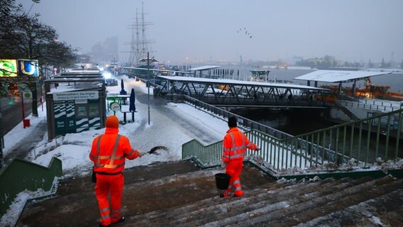 Zwei Mitarbeiter der Stadtreinigung Hamburg räumen und streuen eine Treppe an den Landungsbrücken am Hamburger Hafen. © Christian Charisius/dpa Foto: dpa