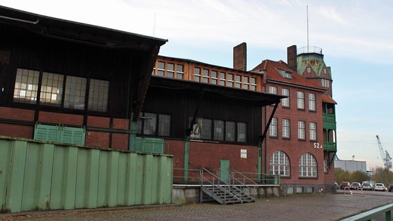 Das Endgebäude einer Schuppenanlage im historischen Teil des Hamburger Hafens auf dem Kleinen Grasbrook steht hinter einer Flutschutzmauer. © NDR Foto: Daniel Sprenger