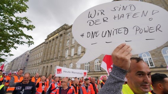 Hafen-Beschäftigte mit Verdi-Flaggen und einem Plakat «Wir sind der Hafen! #One United Power» demonstrieren in der Innenstadt vor der Zentrale der Reederei Hapag-Lloyd. © picture alliance/dpa | Marcus Brandt Foto: Marcus Brandt