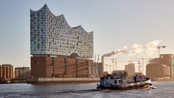 Ein Kahn mit der Aufschrift "Hamburg" fährt auf der Elbe im Hafen an der Elbphilharmonie flussaufwärts vorbei. © picture alliance / dpa Foto: Georg Wendt