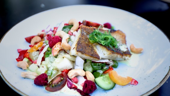Ein Stück Fisch wird auf einem Teller mit Salat angerichtet © NDR Foto: Dave Hänsel