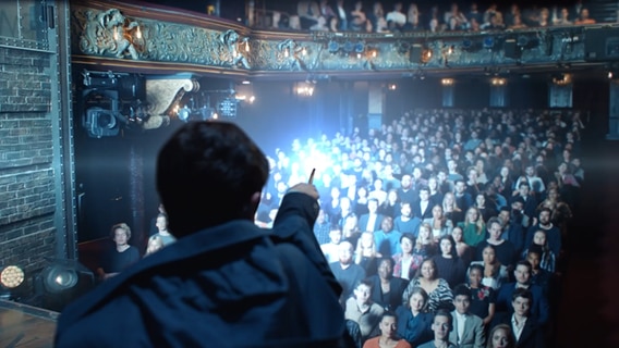 Eine Szene aus dem Theaterstück "Harry Potter und das verwunschene Kind" zeigt einen Darsteller und mehrere Zuschauer. © Mehr-BB Entertainment GmbH Foto: Screenshot