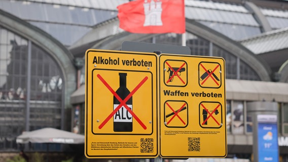Ein Hinweisschild zum Alkoholverbot ist neben einem Verbotsschild für Waffen am Hachmannplatz vor dem Hauptbahnhof. © dpa Foto: Christian Charisius