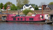 Das pink-farbene Hausboot, in dem eine 58 Jahre alte Frau tot aufgefunden worden war, liegt an einem Steg im Holzhafen im Hamburger Stadtteil Moorfleet. © picture alliance / dpa Foto: Marcus Brandt