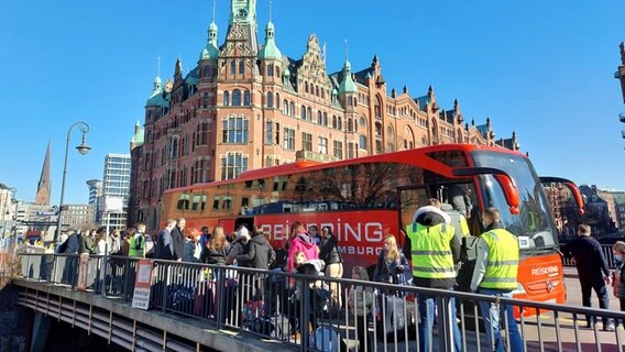 Vor einem roten Reisebus in der Hafencity stehen aus der Ukraine geflüchtete Menschen, die die HHLA nach Hamburg gebracht hat. © NDR / Dietrich Lehmann Foto: Dietrich Lehmann