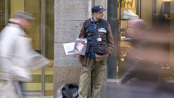 Ein Hinz&Kunzt-Verkäufer steht mit einer Ausgabe des Hamburger Strassenmagazins an einer Straße. © IMAGO / epd Foto: IMAGO / epd