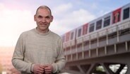 Ole Wackermann steht vor einem Foto einer Hochbahn. © NDR 