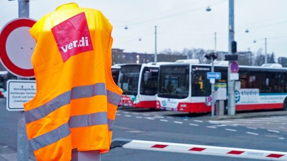 Stehende Busse der Hamburger Hochbahn sind im Hintergrund zu sehen. Im Vordergrund hängt eine Weste mit dem Logo der Gewerkschaft ver.di. © picture alliance 