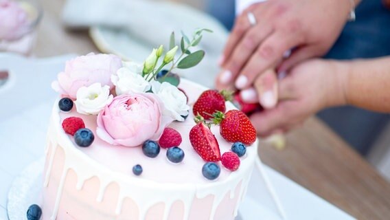 Ein Brautpaar schneidet eine Torte bei der Hochzeitsfeier an. © Hauke-Christian Dittrich Foto: dpa-Bildfunk