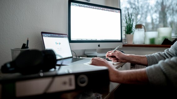 Ein Mann sitzt mit einem Laptop und einem Bildschirm an einem Tisch vor einem Fenster im Homeoffice. © picture alliance/dpa Foto: Fabian Strauch