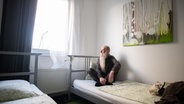 Ein Obdachloser sitzt auf einem Hotelbett © picture alliance/Daniel Reinhardt/dpa Foto: Daniel Reinhardt
