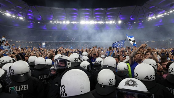 Polizisten stehen vor HSV-Fans, die nach dem Spiel den Rasen gestürmt haben. © Christian Charisius/dpa 