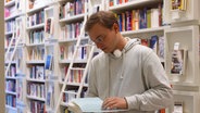 Merlin steht in einer Buchhandlung und sieht sich ein Buch an. © NDR Foto: Frederike Burgdorf