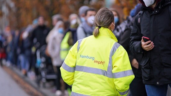 Eine Mitarbeiterin des mobilen Impfteams spricht in Hamburg mit den Menschen in einer Warteschlange. © picture alliance / dpa Foto: Marcus Brandt
