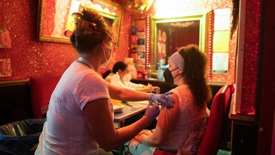 Eine junge Frau lässt sich in der "Wunderbar" nahe der Reeperbahn im Hamburger Stadtteil St. Pauli gegen das Coronavirus impfen. © picture alliance / dpa Foto: Daniel Reinhardt