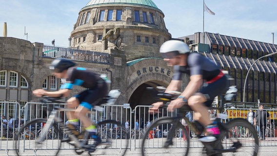 Triathleten fahren beim Ironman in Hamburg an den Landungsbrücken vorbei. © picture alliance/dpa Foto: Georg Wendt