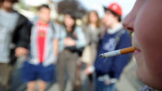 Jugendliche stehen zusammen, einer von ihnen hat eine Zigarette im Mund. © picture alliance / dpa Foto: Philippe Bonnarme