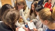 Kinder und Jugendliche machen sich in Hamburg mit den Wahlen vertraut und betrachten Wahlzettel. © NDR Foto: Jörn Straehler-Pohl