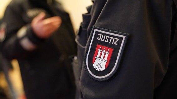 Justizbeamte stehen auf einem Flur vor einem Sitzungssaal im Hamburger Strafjustizgebäude. © picture alliance/dpa Foto: Marcus Brandt