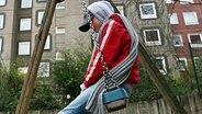 Ein Mädchen sitzt auf einer Schaukel auf einem Spielplatz vor Hochhäusern im Hamburger Stadtteil Billstedt. © dpa - Report Foto: Kay Nietfeld