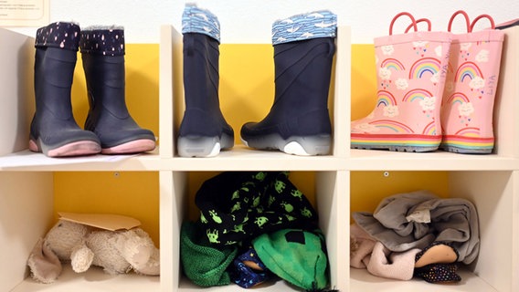 In einer Kita sind Kinderstiefel, ein Stofftier und Kinderkleidung in einem Regal untergebracht. © Uli Deck/dpa 