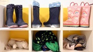 In einer Kita sind Kinderstiefel, ein Stofftier und Kinderkleidung in einem Regal untergebracht. © Uli Deck/dpa 