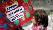 Ein Mädchen steht neben einem Plakat mit der Aufschrift "Streik beenden jetzt".  Foto: Axel Heimken
