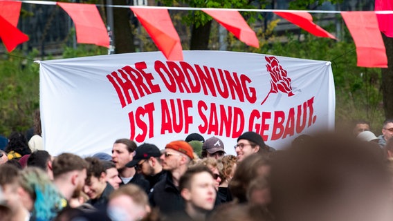 Teilnehmende des linksextremen "Klassenfestes" stehen im Schanzenviertel und halten ein Banner mit der Aufschrift "Ihre Ordnung ist auf Sand gebaut". © dpa Foto: Daniel Bockwoldt