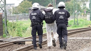 Ein Klimaaktivist, der bei einem Protest auf Gleisen in Hamburg-Wilhelmsburg teilgenommen hat, wird in Gewahrsam genommen. © picture alliance/dpa Foto: Bodo Marks