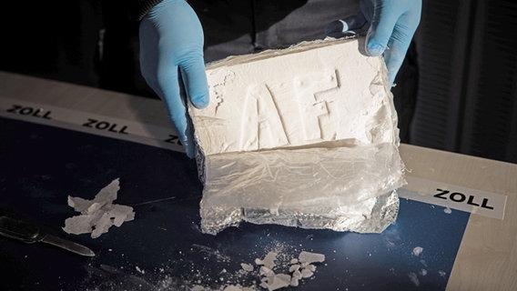 Ein Zollbeamter präsentiert gepresstes und hoch konzentriertes Kokain aus einem großen Kokainfund im Rahmen einer Pressekonferenz des Zoll Hamburg. © dpa Foto: Christian Charisius