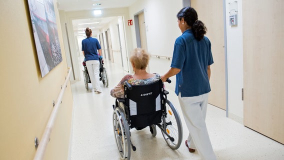 Zwei Pflegerinnen schieben im Asklepios Klinikum Wandsbek Patienten mit Rollstühlen durch einen Flur. © picture alliance / dpa 