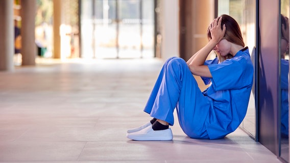 Eine Krankenschwester sitzt auf dem Boden und hält sich die Hände vors Gesicht. © picture alliance / Shotshop | Monkey Business 2 