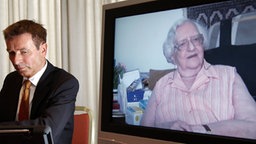 Roger Kusch neben einem TV-Bildschirm, auf dem die verstorbene Frau aus Würzburg zu sehen ist. © dpa Foto: Marcus Brandt