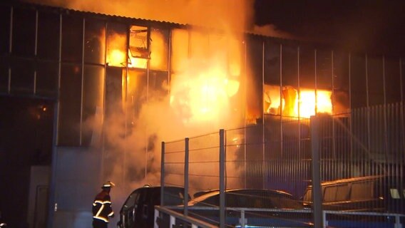 Eine Lagerhall in Hamm steht in Flammen. Das Feuer schlägt aus den Fenstern. Feuerwehrmänner löschen.  Foto: tv news kontor