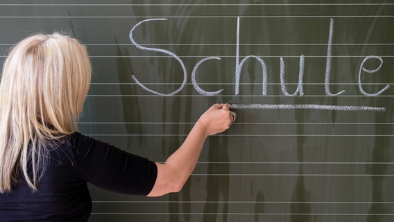 Eine Lehrerin schreibt das Wort "Schule" auf eine Schultafel in einem Klassenzimmer. © picture alliance / dpa Foto: Axel Heimken